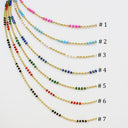 Seven gold beaded chains labeled #1 through #7 arranged in a fan shape on a white background, each featuring different colored bead accents including pink, light blue, white, turquoise, green, red, and black.