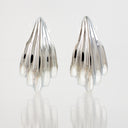 A pair of silver-toned, sculptural hoop earrings with a ribbed, organic texture, displayed on a reflective white surface against a light gray background.