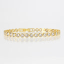 A yellow gold tennis bracelet featuring round-cut clear gemstones in bezel settings, displayed on a clean white reflective surface.