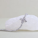 A silver-toned bracelet with a four-leaf clover motif set with clear stones, draped over a white crystal rock on a light beige background.