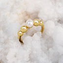 A gold ring featuring a row of polished gold beads with a single white pearl, displayed on a bed of white salt crystals.