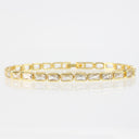 A gold tennis bracelet featuring rectangular clear baguette-cut stones in a row, displayed on a reflective white surface against a light gray background.