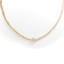 A delicate gold tennis necklace featuring a central round-cut diamond pendant, with smaller diamonds set along the chain, shown against a plain white background.