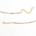 A gold chain bracelet featuring alternating light purple and clear faceted beads with polished gold cylindrical spacers, displayed on a clean white background.