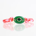 A red and white patterned braided cord bracelet with a central green oval stone and a small green gemstone in the middle, set against a white background with a soft reflection.