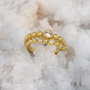 A gold beaded ring with a central round clear gemstone and smaller clear stones, displayed on a bed of white salt crystals.