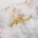 A pair of gold beaded rings with clear gemstones, displayed on a white crystal geode.