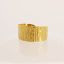 A wide, polished gold cuff bracelet with a vertically textured, wavy surface, displayed on a clean white reflective surface.