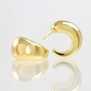 A pair of polished gold crescent-shaped hoop earrings displayed on a reflective white surface against a light gray background.