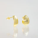 A pair of gold-colored textured stud earrings with a ribbed, wave-like pattern, displayed on a reflective white surface against a light gray background.