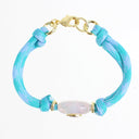 A braided rope bracelet in light blue and turquoise with gold-toned hardware, featuring a central iridescent white bead, photographed on a plain white background.