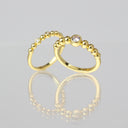 Two gold beaded rings with clear gemstones, displayed on a reflective light gray surface.