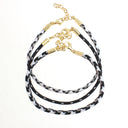Three layered cord bracelets with a black and white speckled pattern, gold-tone metal caps, and gold chain clasps, displayed on a clean white background.