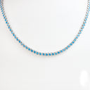 A silver tennis necklace featuring small round blue turquoise-like stones, displayed on a clean white background.