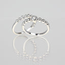 Two silver beaded rings with a small clear gemstone on the front ring, displayed on a reflective light gray surface.
