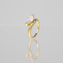 A gold ring with a marquise-cut clear gemstone in a prong setting, shown on a reflective light gray surface.