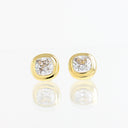 A pair of gold stud earrings with cushion-cut clear gemstones, displayed on a reflective white surface.