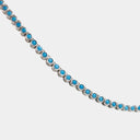 A silver tennis necklace featuring round, bright blue turquoise-like gemstones set in a silver-toned metal, shown against a light gray background.