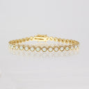 A yellow gold tennis bracelet featuring round bezel-set white opal stones, displayed on a clean white reflective surface.