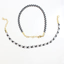 A braided black and white rope choker necklace with gold-tone metal hardware, including a lobster clasp, extension chain, and toggle clasp, displayed on a clean white background.
