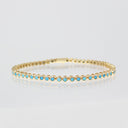A gold tennis bracelet featuring a row of small round light blue turquoise-like gemstones, displayed on a clean white reflective surface.