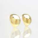 A pair of polished gold teardrop-shaped stud earrings on a reflective white surface against a light gray background.