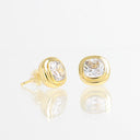 A pair of gold stud earrings with cushion-cut clear gemstones, displayed on a reflective white surface against a white background.