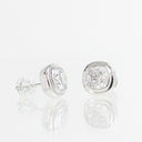 A pair of silver stud earrings with cushion-cut clear gemstones, shown on a reflective white surface against a white background.
