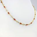 A gold chain necklace displayed on a white mannequin bust, featuring marquise-cut orange-red stones and small clear round stones set along the link design.