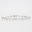 A silver tennis bracelet featuring a row of clear baguette-cut gemstones, displayed on a reflective white surface against a light gray background.