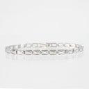 A silver-toned tennis bracelet featuring rectangular baguette-cut clear stones, displayed on a clean white reflective surface.