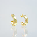 A pair of gold hoop earrings with small colorful gemstone accents, displayed on a reflective light gray surface.