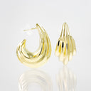 A pair of polished yellow gold earrings on a reflective white surface. One earring is shown from the front, displaying a smooth, curved crescent-like shape, while the other is shown from the side, revealing a textured, ribbed design.