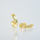 A pair of gold huggie hoop earrings decorated with small multicolored gemstones, displayed on a reflective white surface against a light gray background.