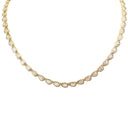 A gold tennis necklace featuring small teardrop-shaped clear gemstones in bezel settings, arranged in a curved line on a plain white background.