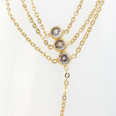 A gold multi-layer necklace with three round bezel-set clear stones on a white background.