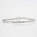 A silver tennis bracelet with a continuous link design and a clasp closure, displayed on a clean white reflective surface.