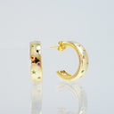 A pair of gold hoop earrings decorated with small colorful gemstones, shown on a reflective light gray background.