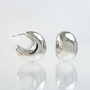 A pair of polished silver crescent-shaped hoop earrings, one shown from the side with a clear plastic earbud tip and the other from the front, displayed on a reflective white surface.