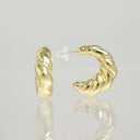 A pair of polished yellow gold hoop earrings with a twisted rope texture, shown on a reflective light gray surface. One earring is displayed upright, and the other is shown from the side/back with a clear plastic post and backing.
