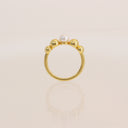 A gold ring featuring a circular band with five polished gold beads surrounding a single white pearl, set against a soft cream background with a faint reflection below.