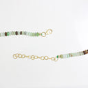 A beaded bracelet with small round beads in shades of green, brown, and white, accented with gold-toned hardware including a lobster clasp and an adjustable chain extender.