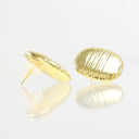 A pair of gold oval stud earrings with a ribbed, textured surface, displayed on a reflective white surface against a white background.