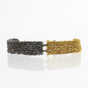A double-ended chain-link bracelet featuring one side in oxidized silver and the other in polished gold, separated by a central cluster of three white pearls, shown on a reflective white surface.
