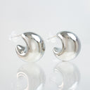 A pair of polished silver crescent-shaped hoop earrings with clear butterfly backings, displayed on a reflective white surface against a light gray background.