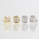 Four rectangular cushion-cut clear gemstone stud earrings in bezel settings, shown in both yellow gold and silver metal finishes on a reflective light gray surface.