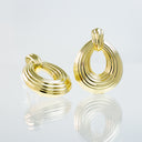 A pair of gold-toned hoop earrings with a textured, ridged circular design, displayed on a reflective white surface.