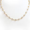 A delicate gold tennis necklace featuring small oval-cut clear gemstones in bezel settings, displayed against a clean white background.