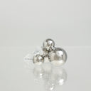 Three metallic silver ball stud earrings with clear plastic backing, arranged on a reflective light gray surface.