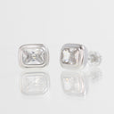 A pair of silver stud earrings with rectangular cushion-cut clear gemstones, shown on a reflective white surface against a light gray background.